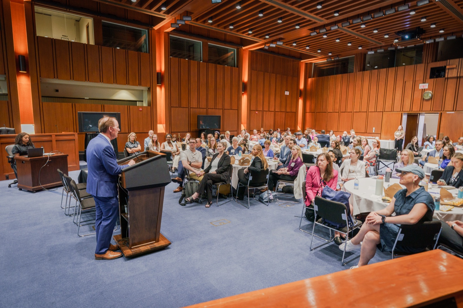 A speaker at a podium addressing a full room of advocates